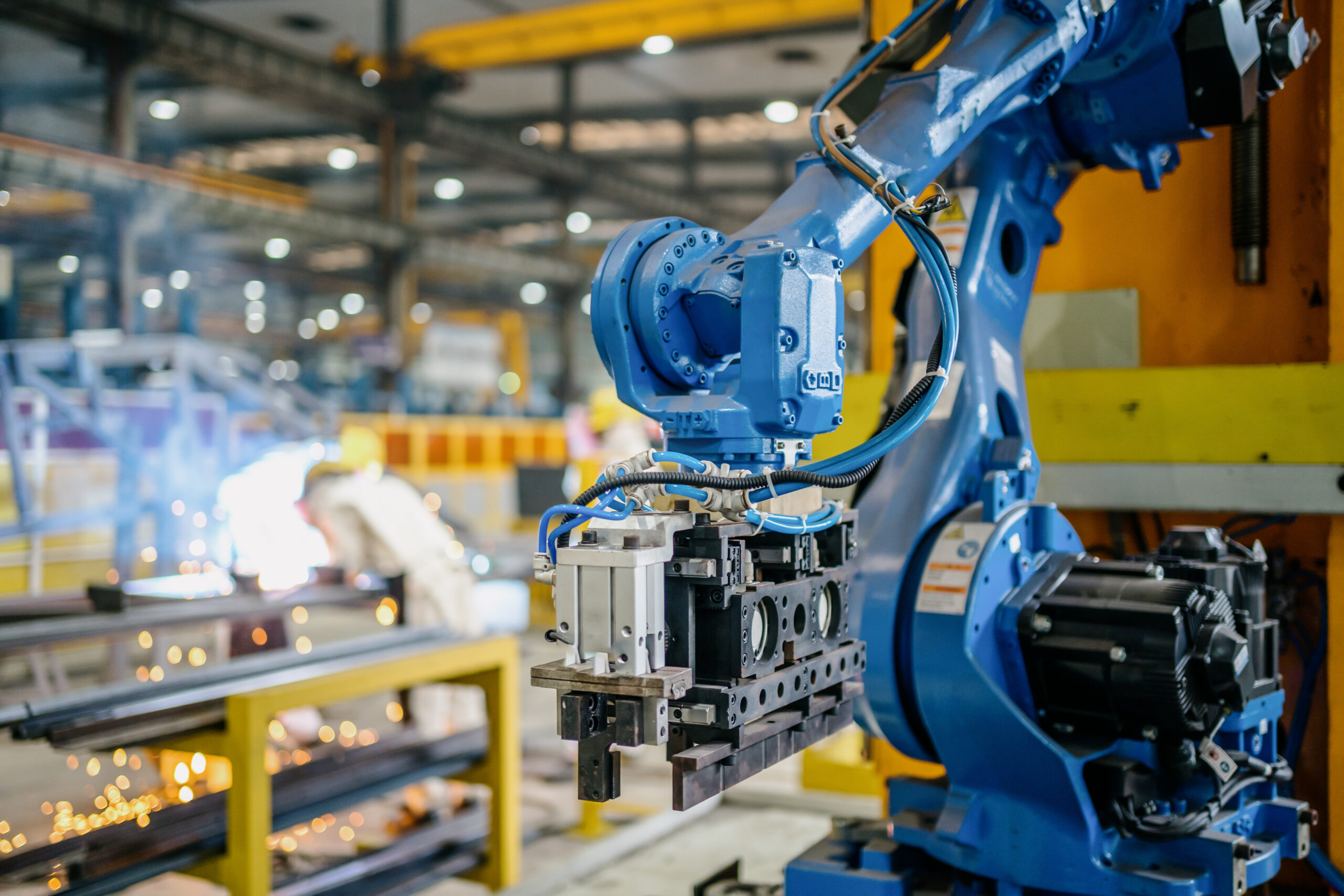 A blue robotic arm moves electronic components on a busy factory floor